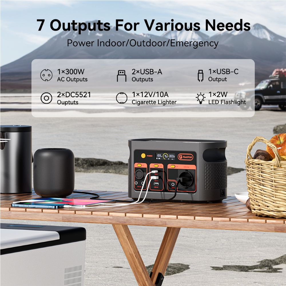 Estación de energía portátil en mesa de madera al aire libre con cables, teléfono y cesta de fruta.