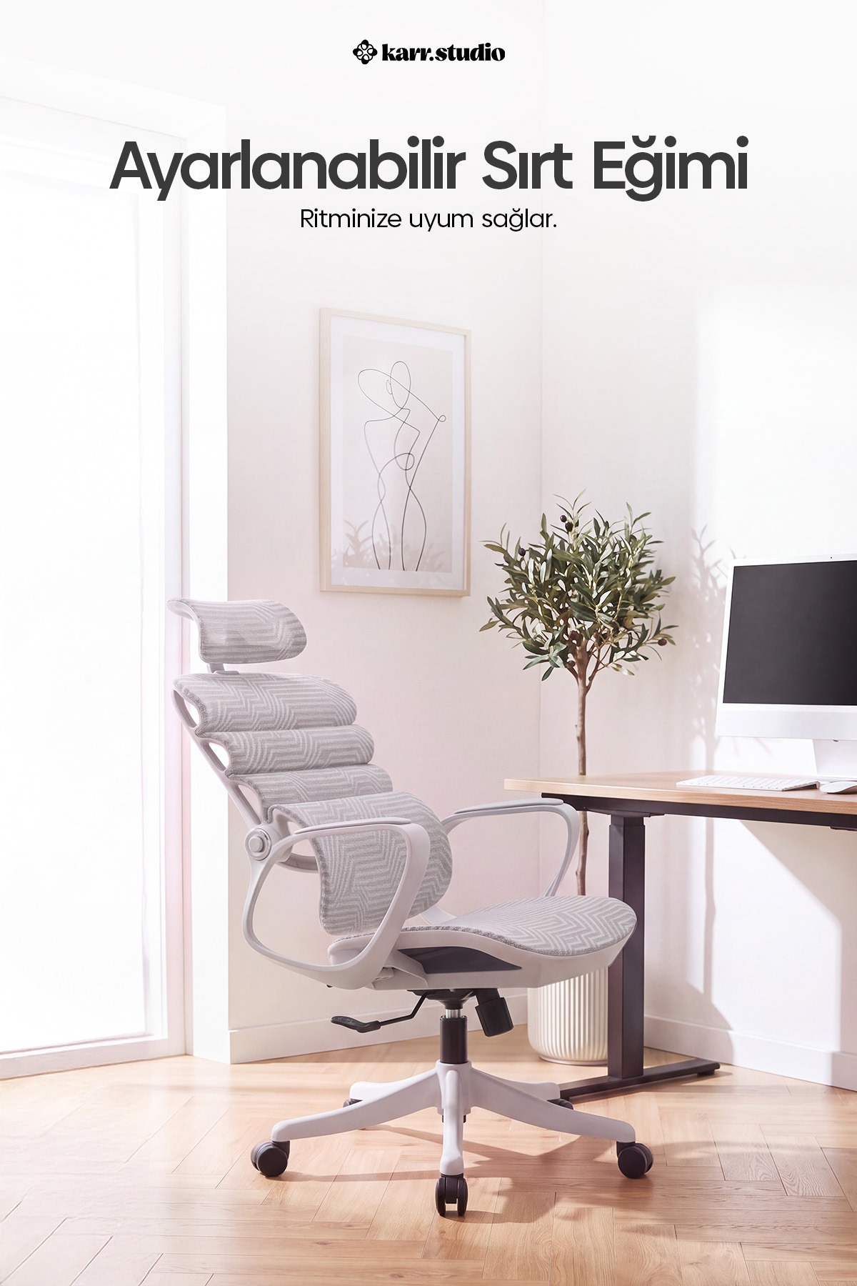 Aydınlık odada masa, saksı bitkisi ve tablo olan ergonomik gri ofis koltuğu.