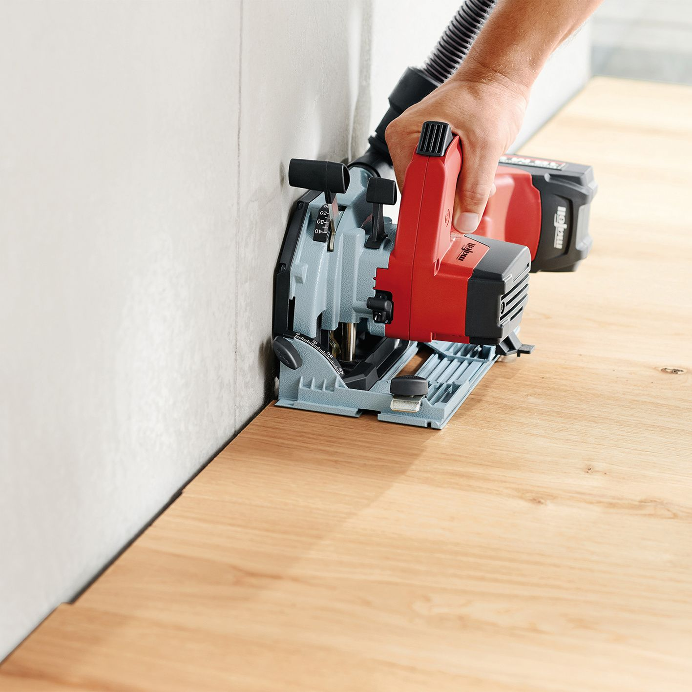 Eine Hand benutzt eine rote und graue Kreissäge, um Holzböden nah an einer Wand zu schneiden.