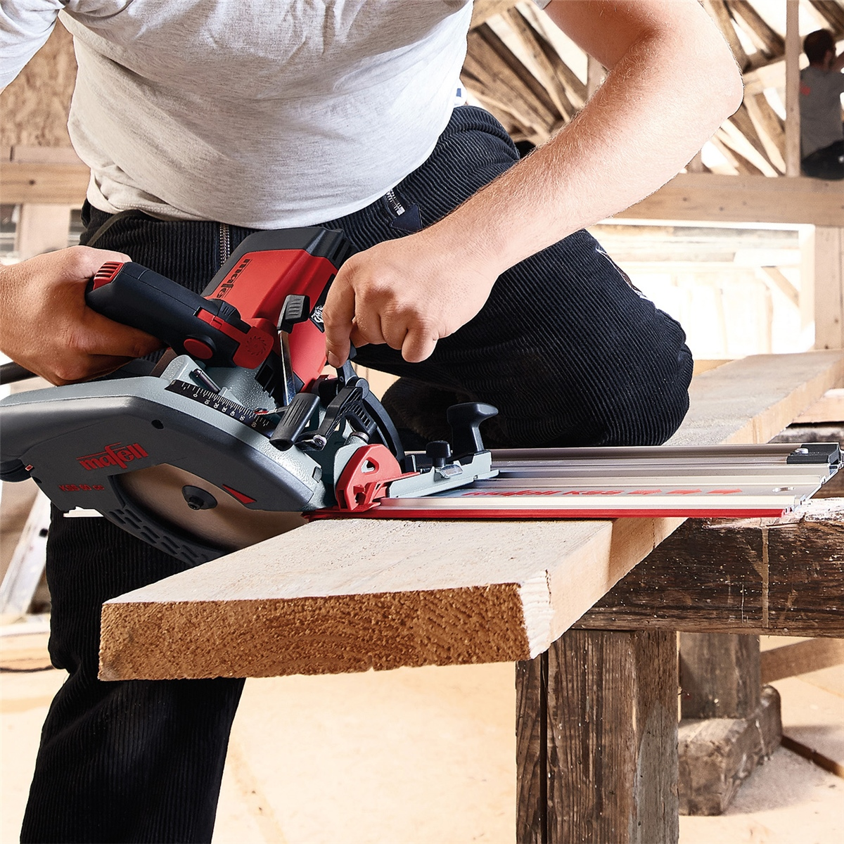 Ein Handwerker schneidet mit einer roten Kreissäge auf einer Führungsschiene ein Holzbrett in einer Werkstatt.