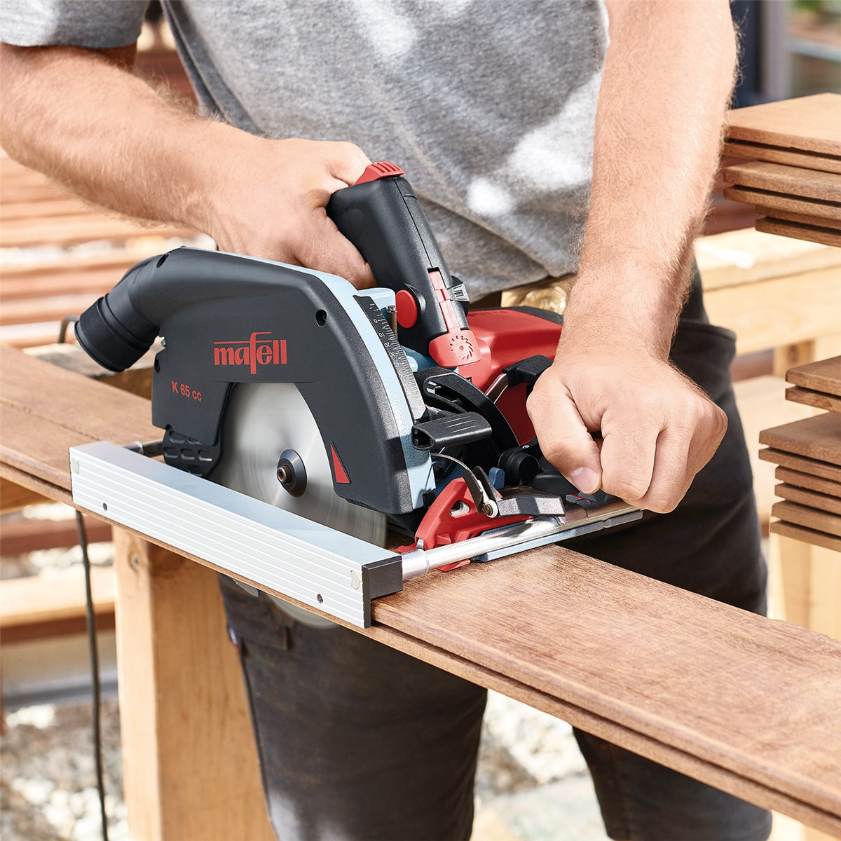 Person schneidet ein Holzbrett mit einer schwarzen und roten Mafell Handkreissäge zu.