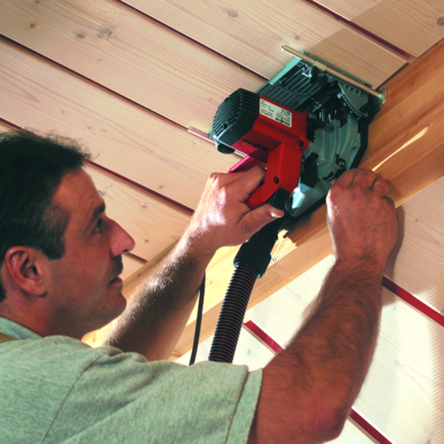 Ein Handwerker schneidet mit einer roten Kreissäge Holzleisten an einer Holzwand.