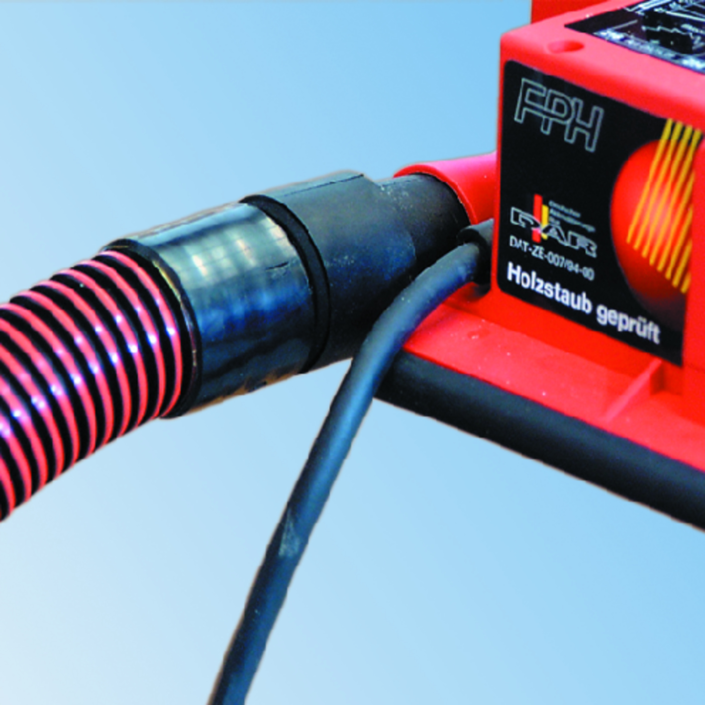 Nahaufnahme eines roten Elektrowerkzeugs mit schwarz gestreiftem Schlauch und Kabel vor blauem Hintergrund.