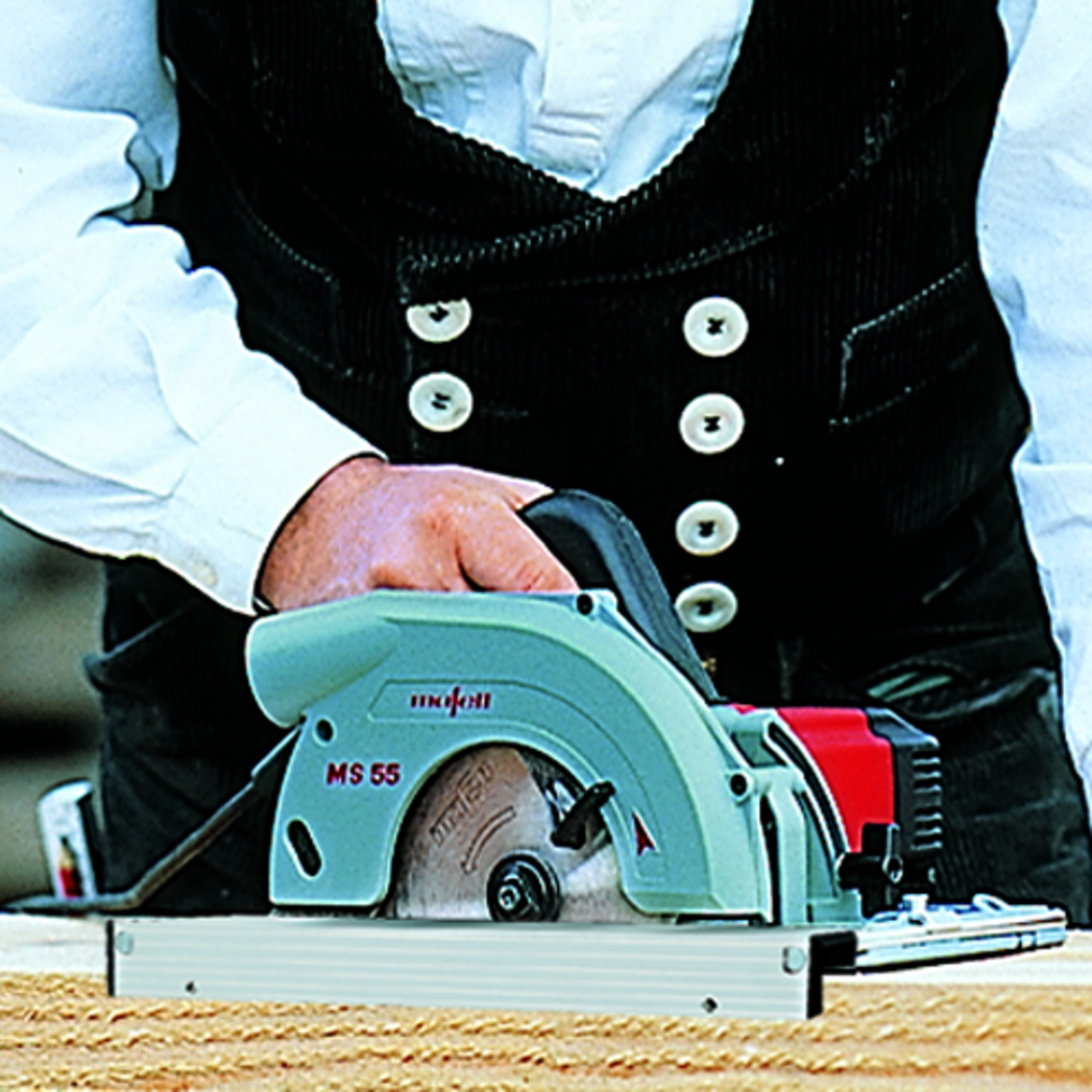 Eine Person in traditioneller Kleidung hält eine grüne MS 55 Kreissäge auf Holz.