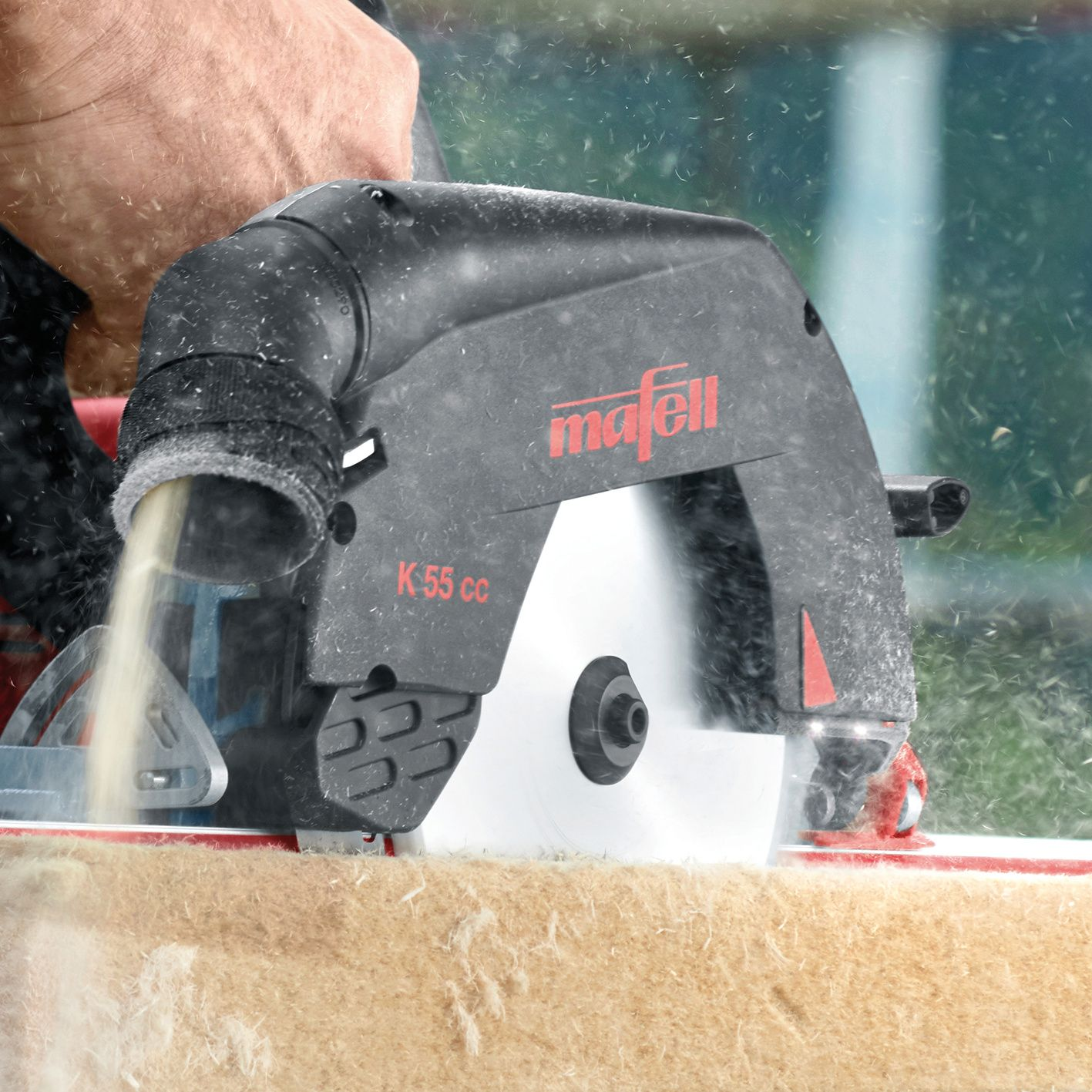 Eine Hand bedient eine schwarze Mafell K 55 cc Kreissäge, die Holz schneidet und Späne auswirft.