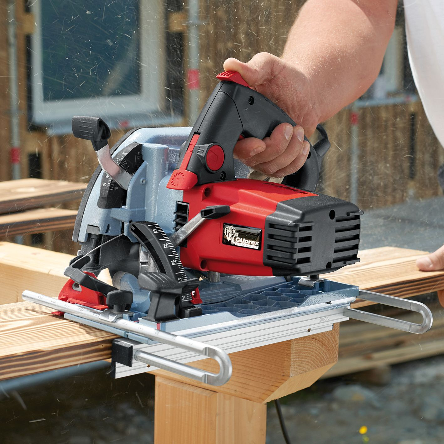 Eine Hand hält eine rot-schwarze Handkreissäge, die ein Holzbrett auf einem Tisch schneidet, während Sägemehl fliegt.