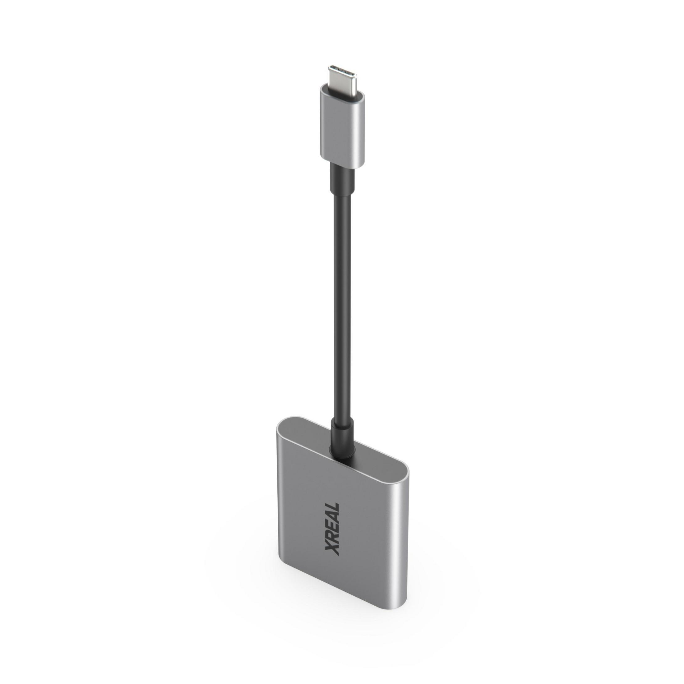 Un adaptador XREAL plateado con cable negro y conector USB-C sobre fondo blanco.