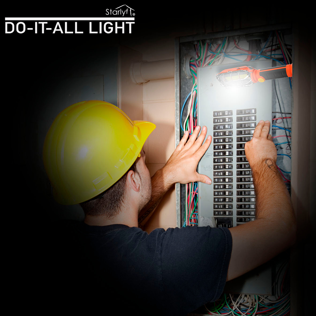 Un lavoratore con elmetto giallo ispeziona un quadro elettrico aperto, illuminato da una luce portatile.
