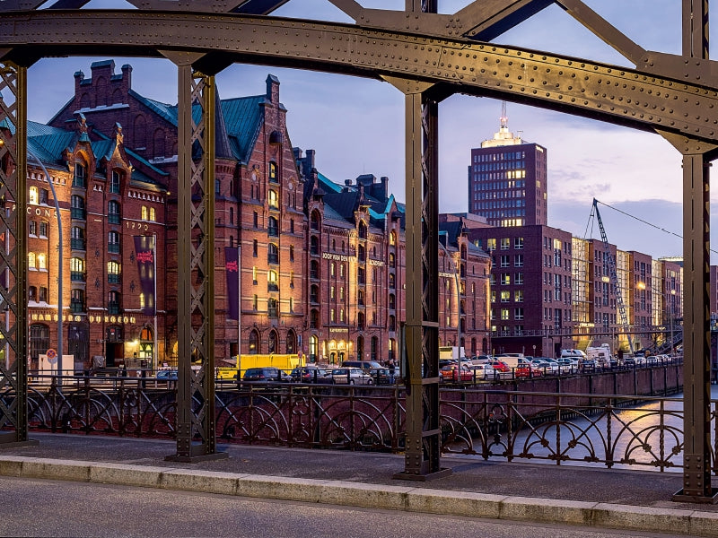 Blick durch einen Metallbrückenrahmen auf historische Backsteingebäude am Kanal in der Dämmerung.
