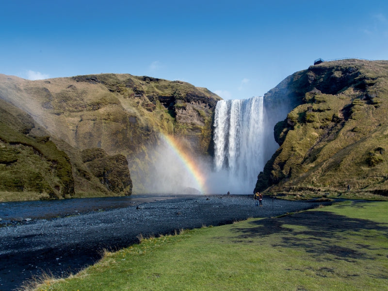 Ein großer Wasserfall stürzt zwischen grünen Klippen herab, mit einem Regenbogen im Sprühnebel.