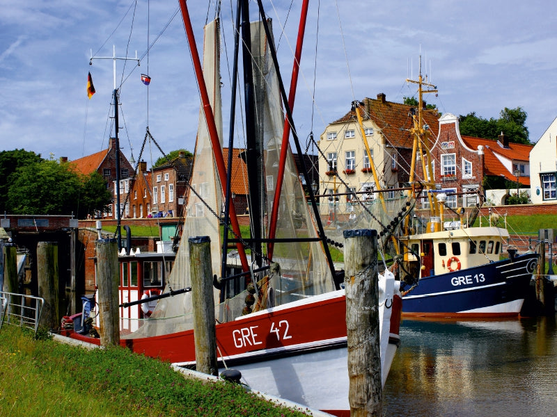 Fischerboote im Hafen vor historischen Backsteinhäusern an einem sonnigen Tag.