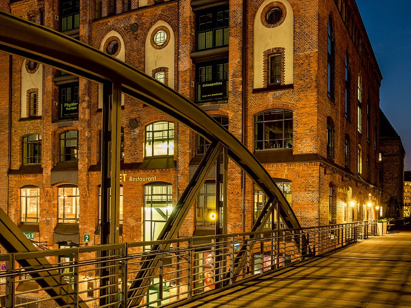 Beleuchtete historische Backsteingebäude und eine Metallbrücke bei Nacht.
