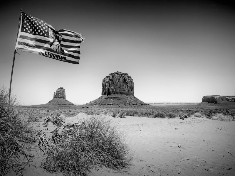 Schwarzweiß-Ansicht einer Wüstenlandschaft mit Tafelbergen und einer amerikanischen Flagge mit dem Wort Geronimo.