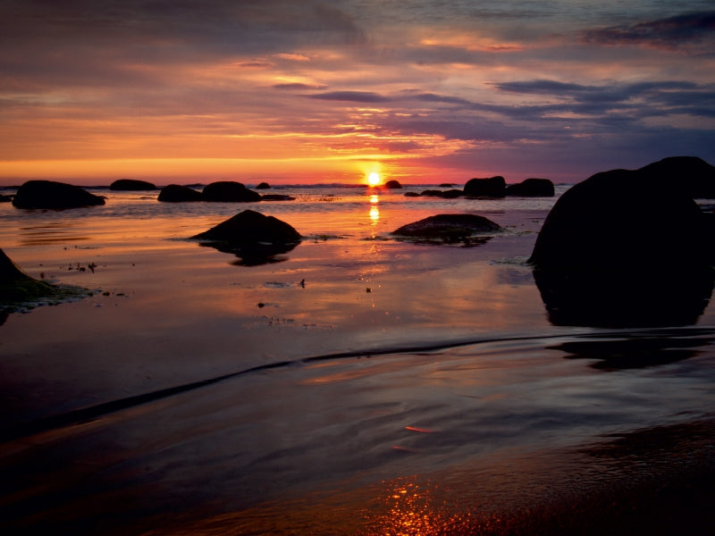 Sonnenuntergang am Meer mit silhouettierten Felsen und orangefarbenem Himmel.