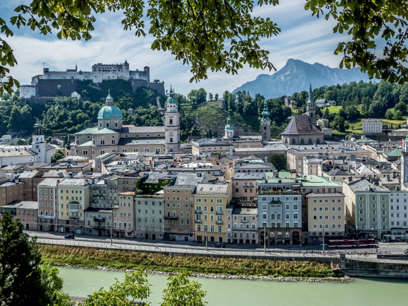 Blick auf Salzburg mit Salzach im Vordergrund, Dom und Festung Hohensalzburg im Hintergrund unter blauem Himmel.