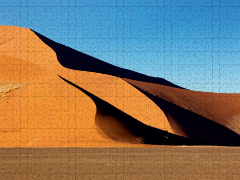 Puzzle mit orangeroten Sanddünen unter blauem Himmel und Schatten.