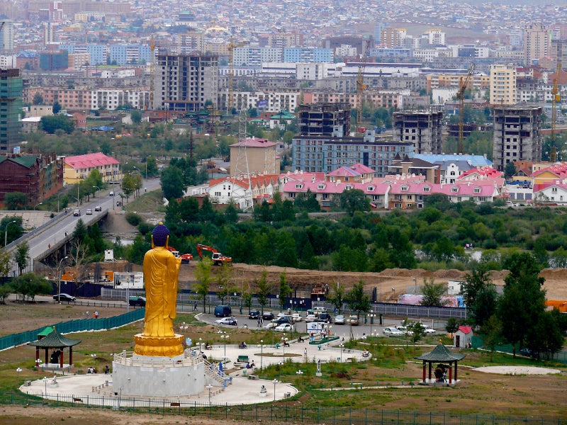 Eine große goldene Buddhastatue in einem Park mit Blick auf eine Stadt.