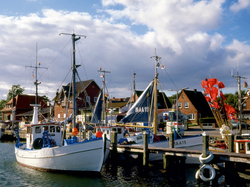 Fischerboote liegen im Hafen vor rosenen Backsteinhäusern unter bewölktem Himmel.