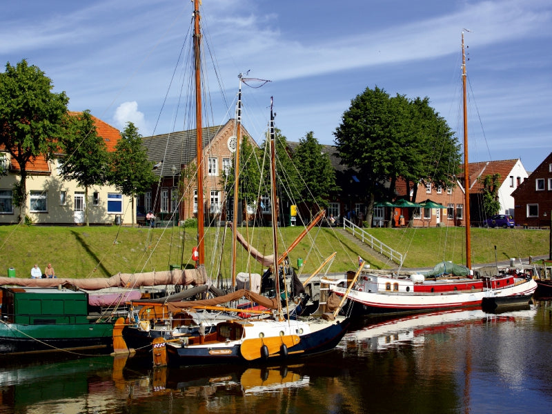 Segelboote an einem grünen Hafenkanal mit historischen Backsteinhäusern und Bäumen.