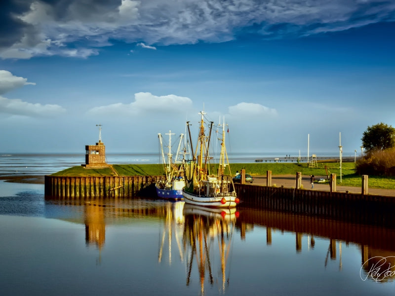 Fischerboote in einem ruhigen Hafen mit Ziegelturm, Holzsteg und Wolkenspiegelung unter blauem Himmel.