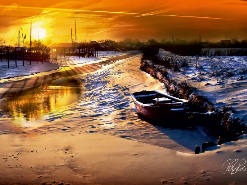 Ein verschneites Ufer mit einem kleinen Boot neben einem Fluss bei Sonnenuntergang.