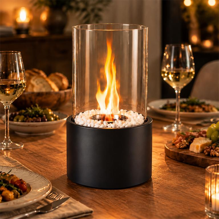 Eine Tisch-Glasfeuerstelle auf einem Holzesstisch mit Weingläsern und Essen im Hintergrund.
