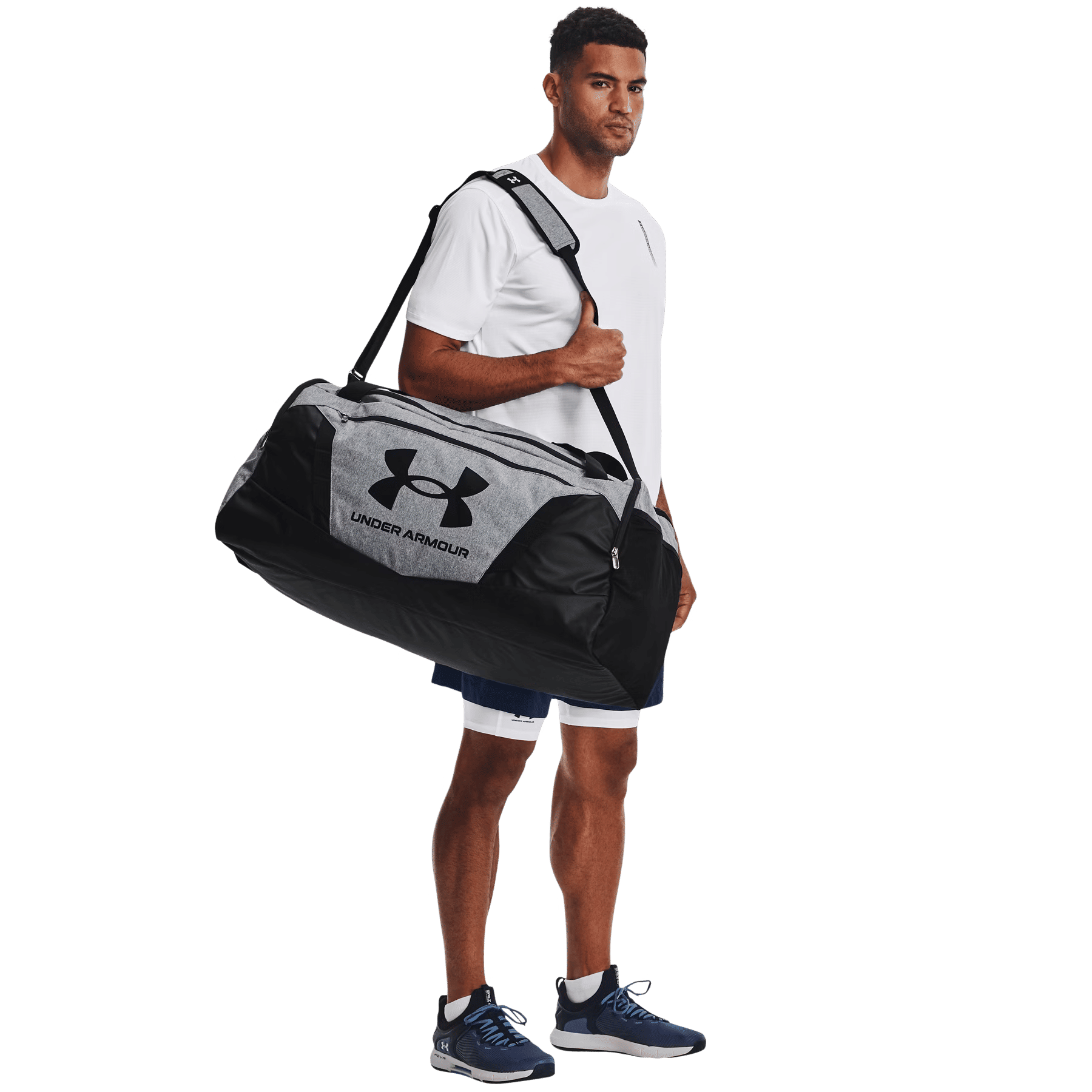 Uomo con maglietta bianca regge una borsa sportiva grigia e nera Under Armour sulla spalla su sfondo nero.