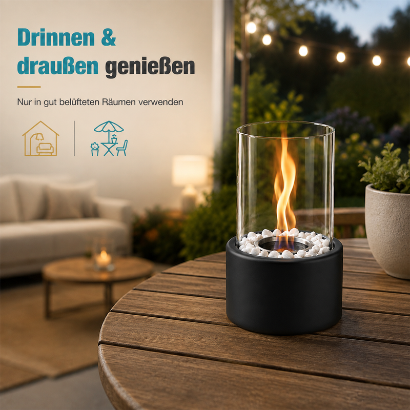 Eine kleine Tischfeuerstelle mit Glaszylinder und Flamme steht auf einem Holztisch, im Hintergrund ein Wohnzimmer.