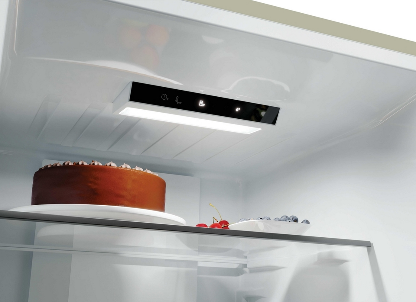 Interno di un frigorifero illuminato con una torta al cioccolato, ciliegie e mirtilli su un ripiano in vetro.