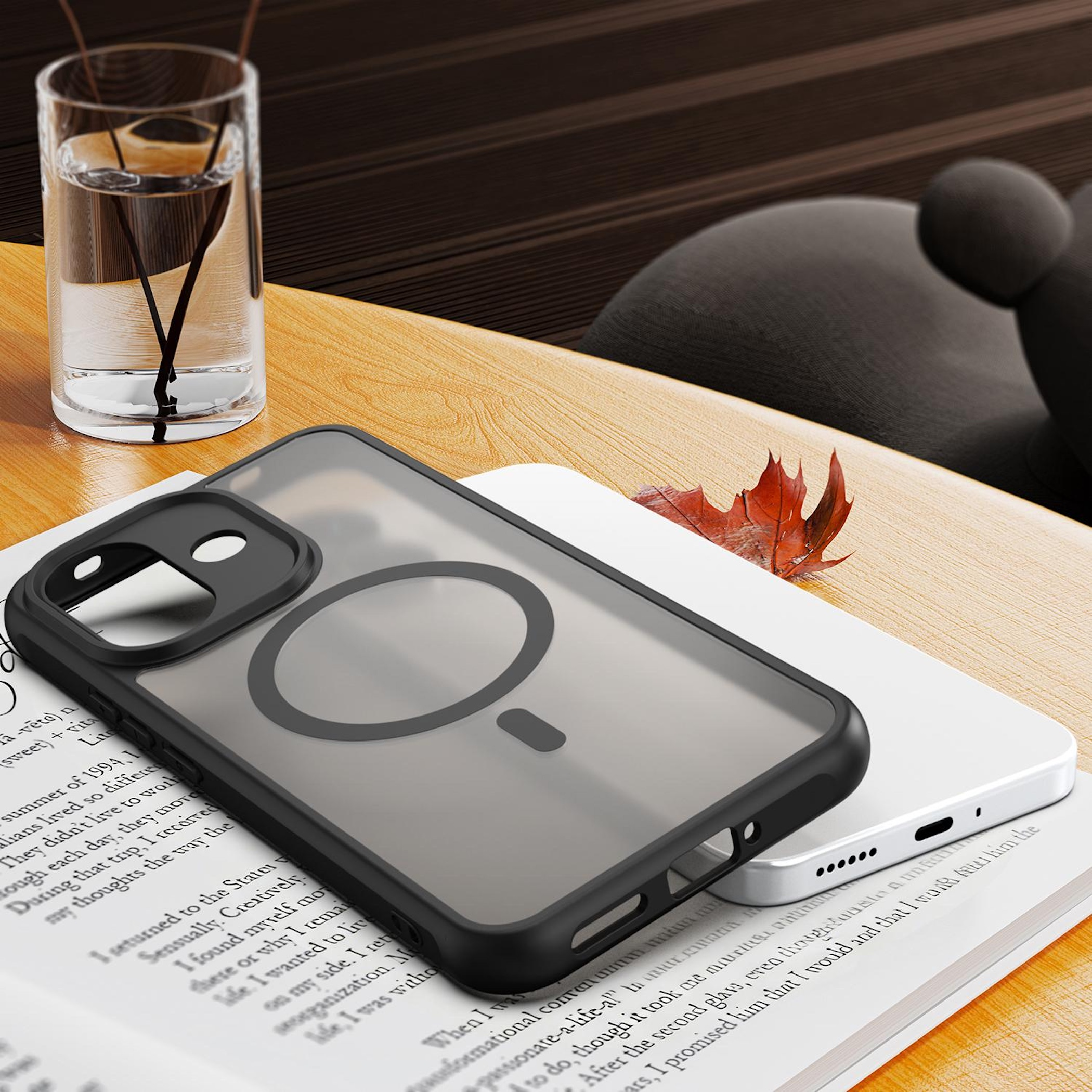 Eine schwarze Smartphone-Hülle liegt auf einem aufgeschlagenen Buch neben einem Glas Wasser auf einem Holztisch.
