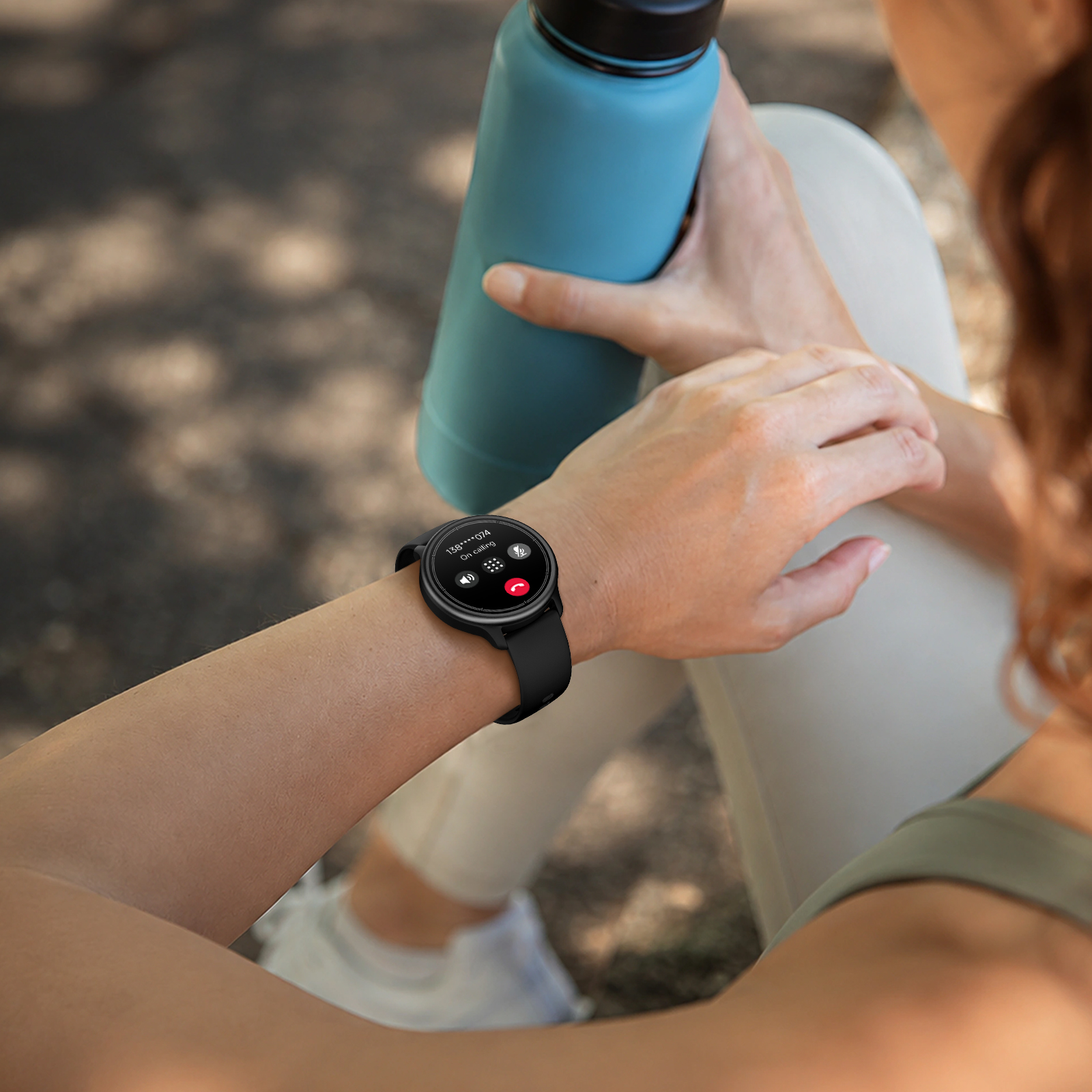 Una mujer en ropa deportiva sostiene una botella azul y mira su reloj inteligente.