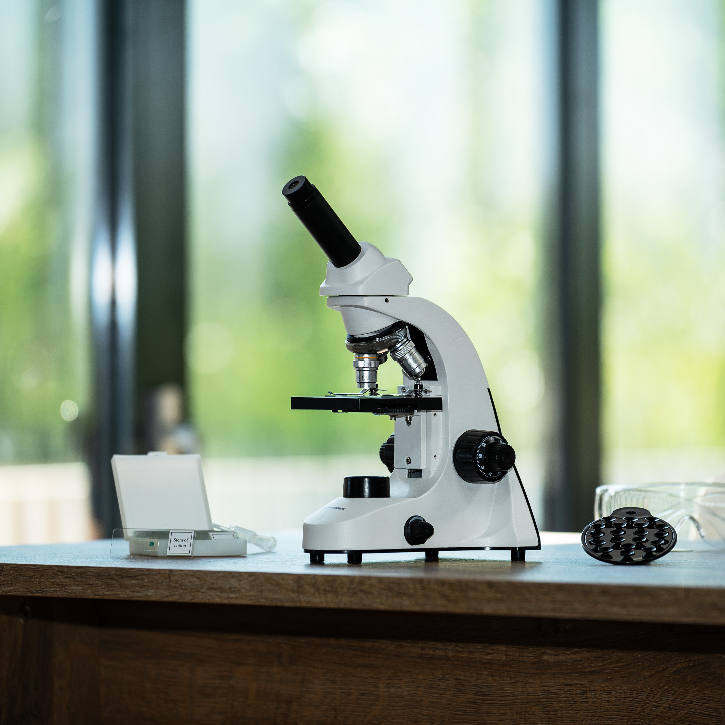 Un microscopio blanco se encuentra sobre una mesa de madera con fondo borroso.