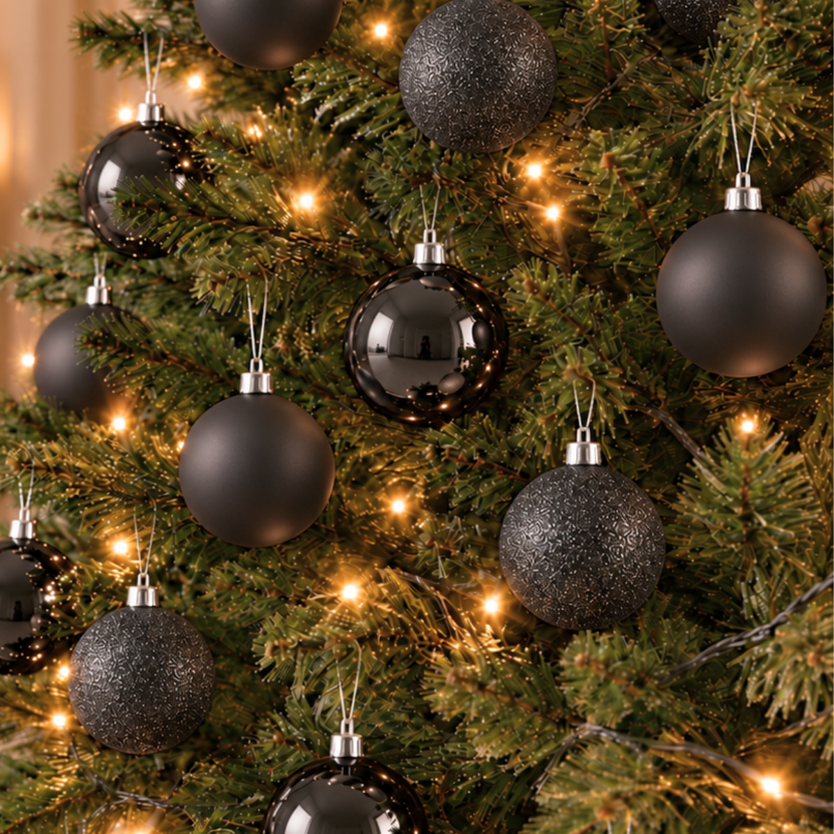 A Christmas tree decorated with black matte, shiny, and textured ornaments amidst warm glowing fairy lights.