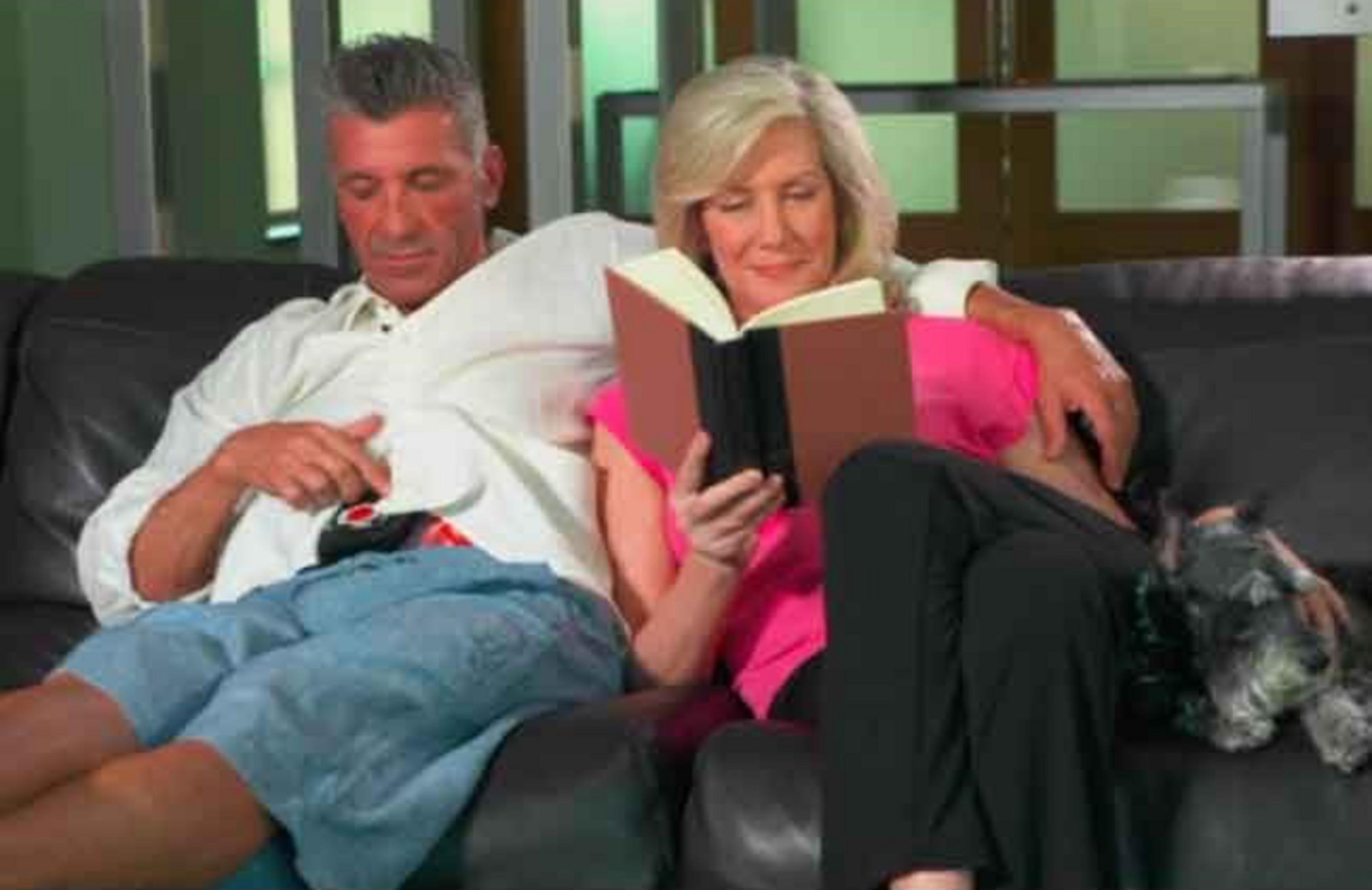 Ein Paar sitzt auf einem Sofa; sie liest ein Buch, er ruht sich daneben aus.