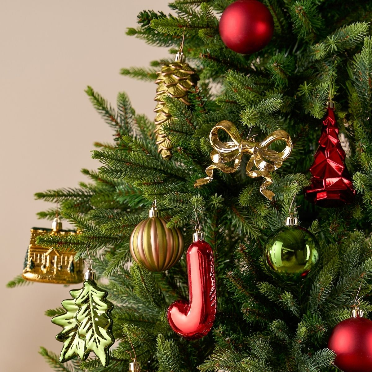 Un sapin de Noël décoré avec des ornements colorés comprenant une boule rouge, un nœud doré, une pomme de pin et une maison.