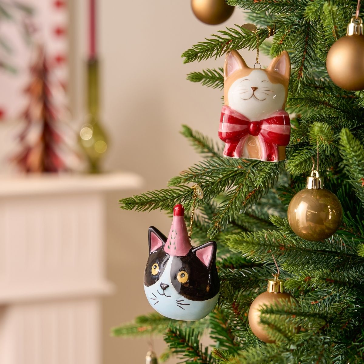 Deux ornements de chat sont suspendus à un sapin de Noël, entourés de boules dorées.