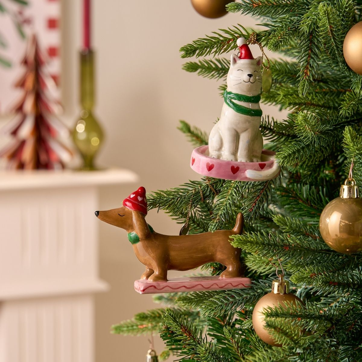 Sapin de Noël avec ornements en céramique : un chat blanc et un teckel portant des bonnets.