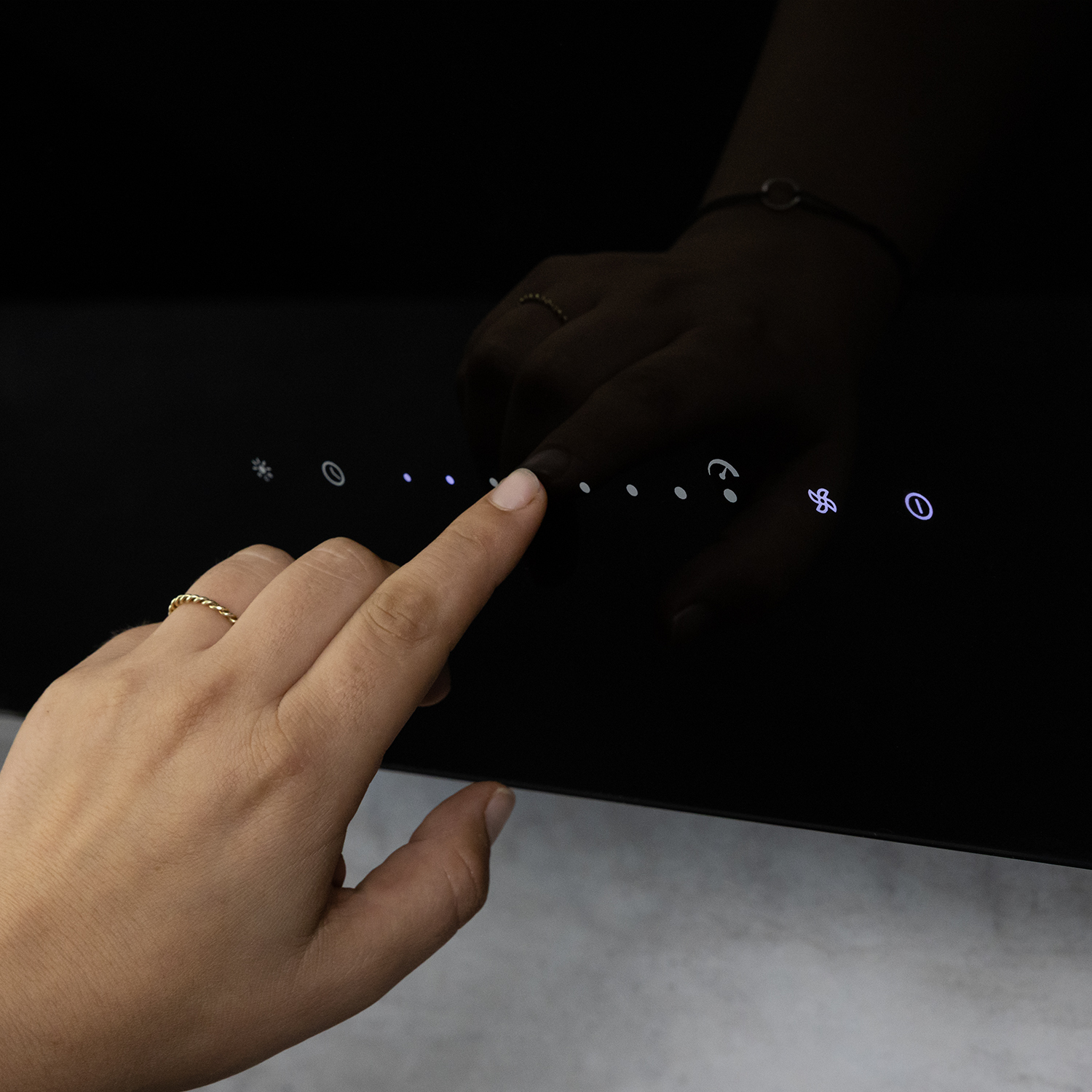 Una mano con un anello d'oro tocca il pannello di controllo touch illuminato di un elettrodomestico nero.
