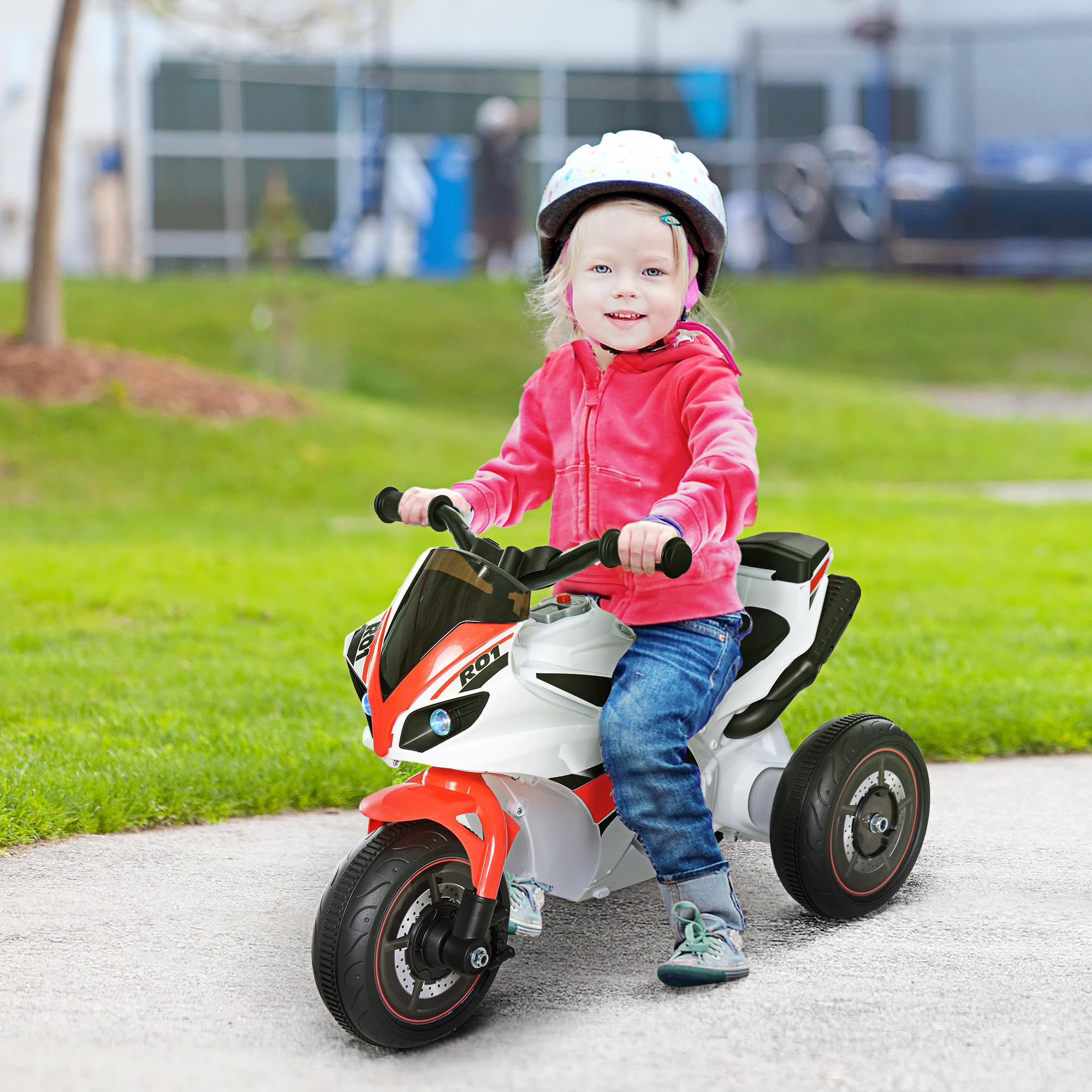 Bambino con casco guida una moto giocattolo rossa e bianca su un sentiero asfaltato.