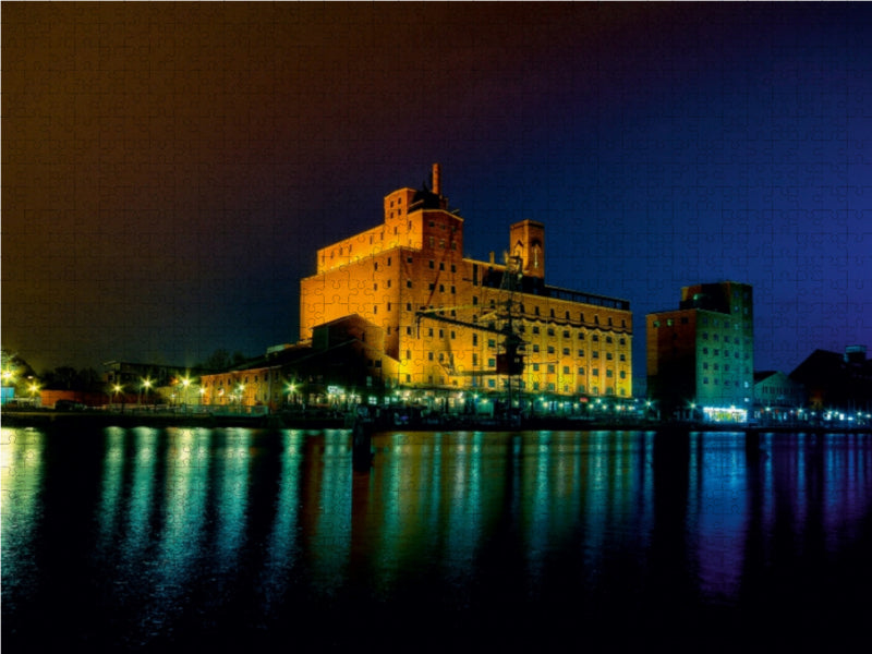 Beleuchtete Gebäude am Wasser bei Nacht spiegeln sich in den dunklen Wellen.