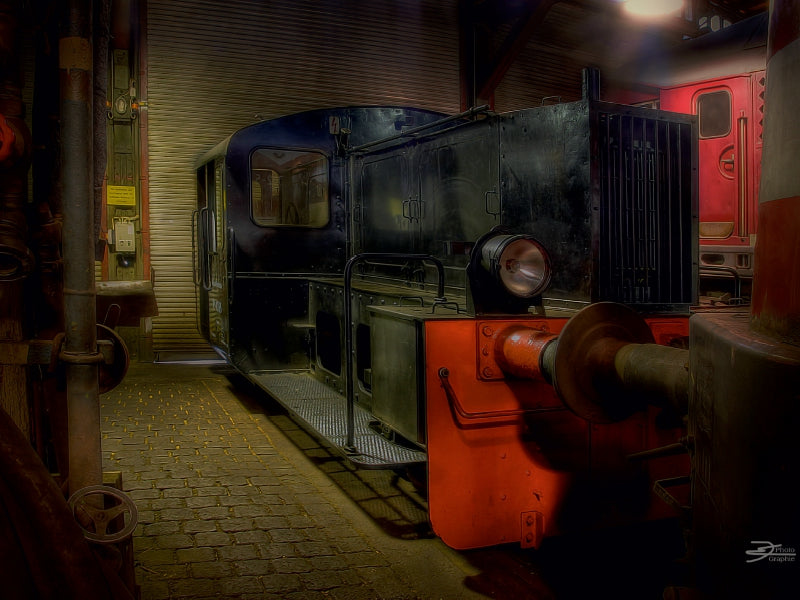 Eine alte schwarze Diesellokomotive mit einem roten Pufferbalken steht im Innenbereich einer Werkstatt.