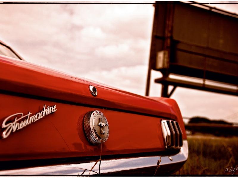 Rückansicht eines roten Oldtimer-Autos vor einem Schild, sepiafarben getönt.