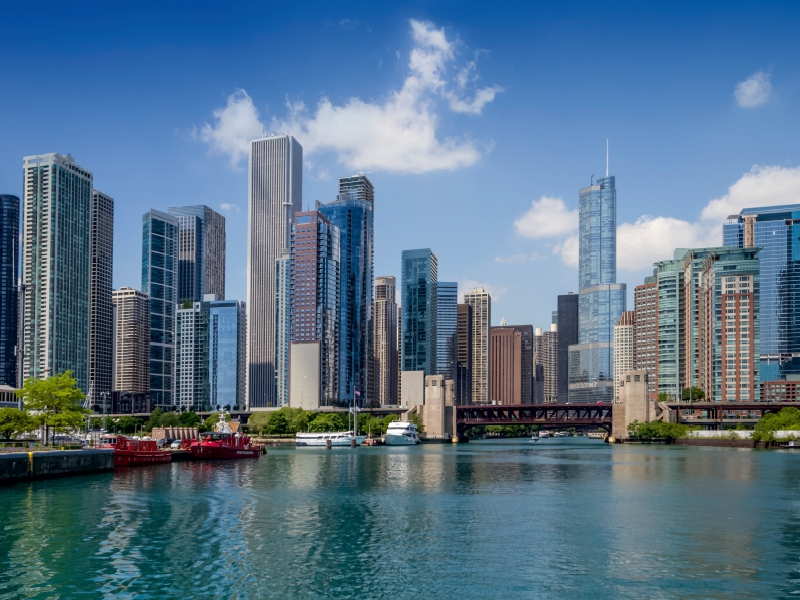 Chicagoer Skyline mit modernen Wolkenkratzern entlang des Chicago River, Brücken und Booten im Vordergrund.