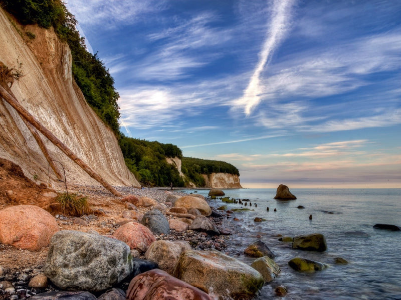 Kreidefelsen an einem steinigen Strand unter blauem Himmel mit leichten Wolken.