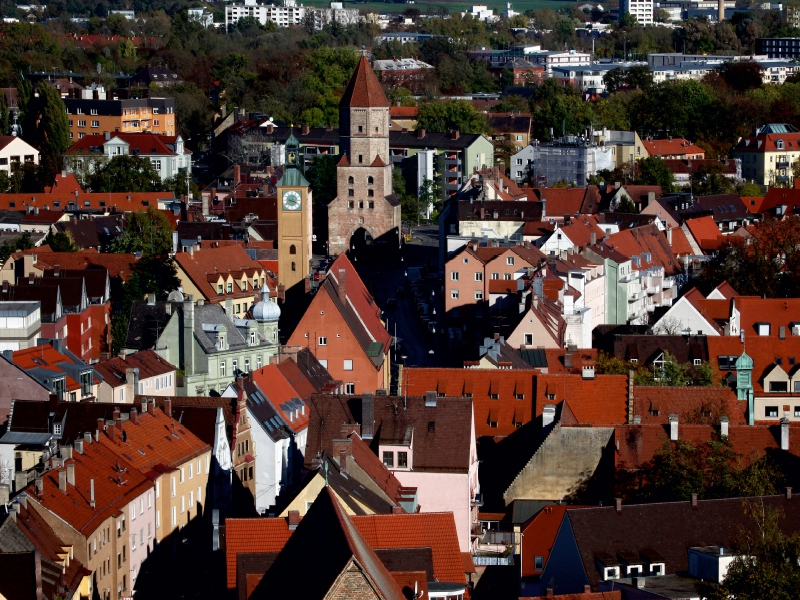 Luftaufnahme einer historischen Stadt mit roten Ziegeldächern, alten Türmen und dichter Bebauung.