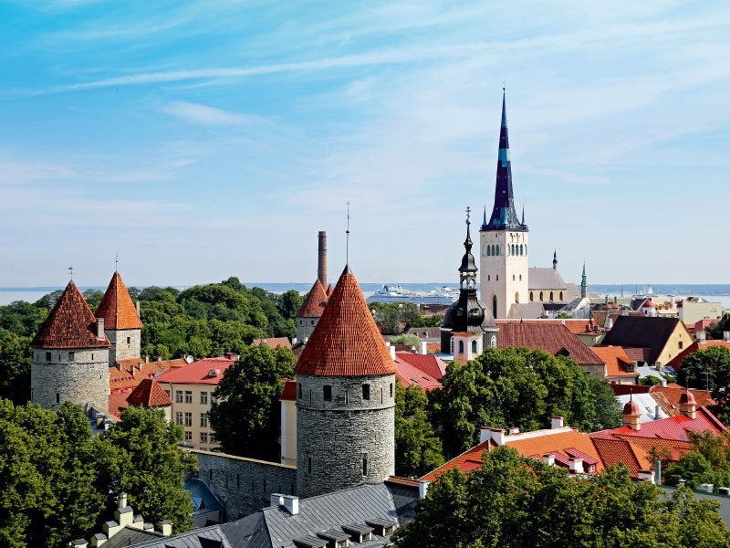 Blick von oben auf die historische Altstadt von Tallinn mit Wehrtürmen, roten Ziegeldächern und einer hohen Kirchturmspitze unter blauem Himmel.