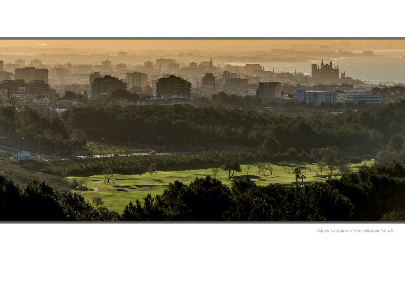 Panoramablick auf einen Golfplatz im Vordergrund und eine neblige Stadt im Hintergrund unter einem goldenen Himmel.