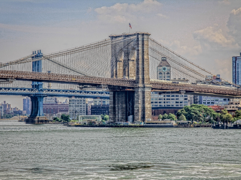 Blick auf die Brooklyn Bridge und die Manhattan Bridge über dem Fluss, mit New Yorker Skyline im Hintergrund.