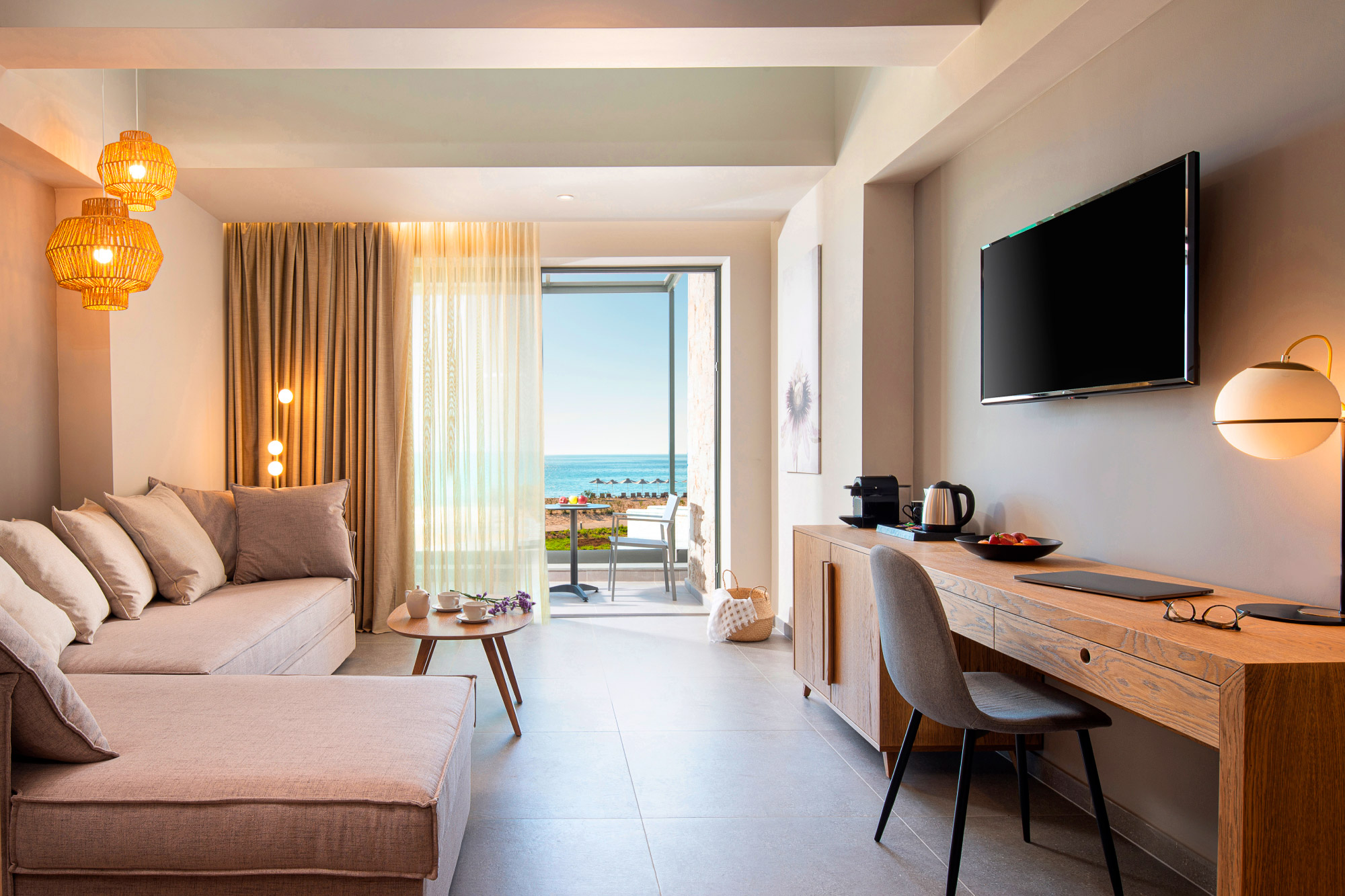 Nowoczesny salon hotelowy z dużą sofą, biurkiem, telewizorem i widokiem na ocean.