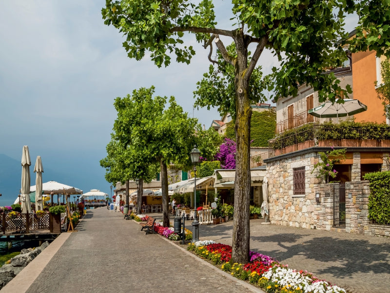 Eine malerische Uferpromenade mit Bäumen, Blumenbeeten und charmanten Steinhäusern an einem See.